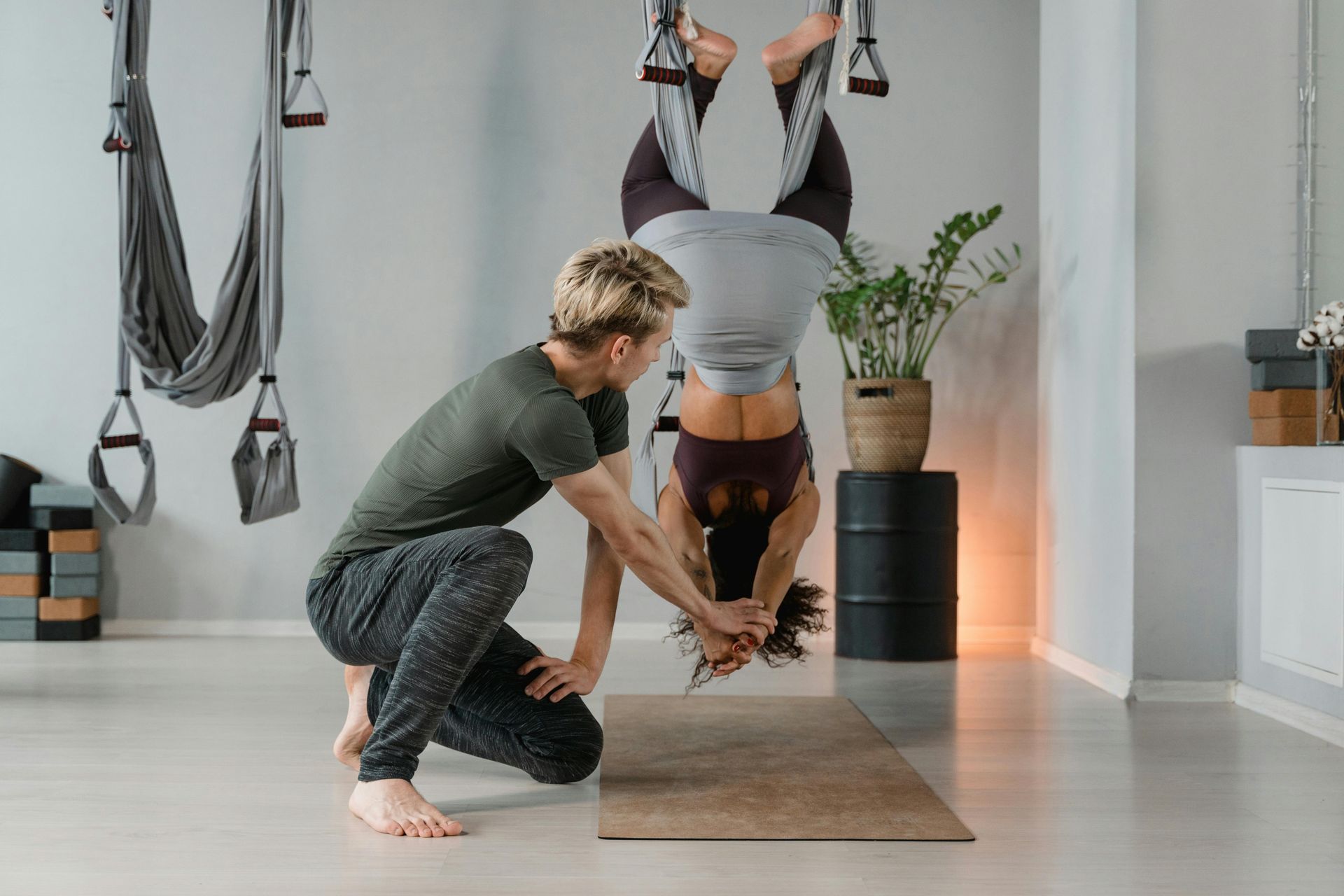 A man is helping a woman do a handstand on a yoga mat.