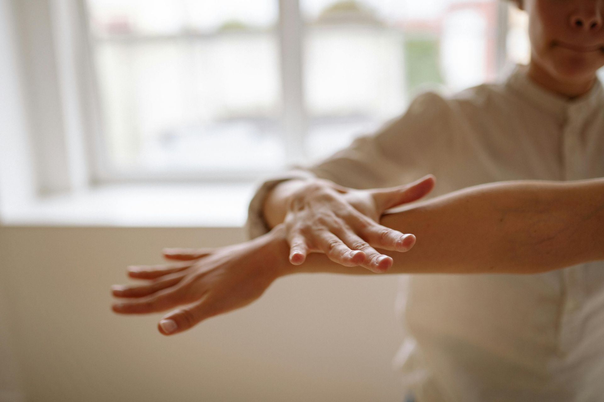 A woman is stretching her arms in front of a window.