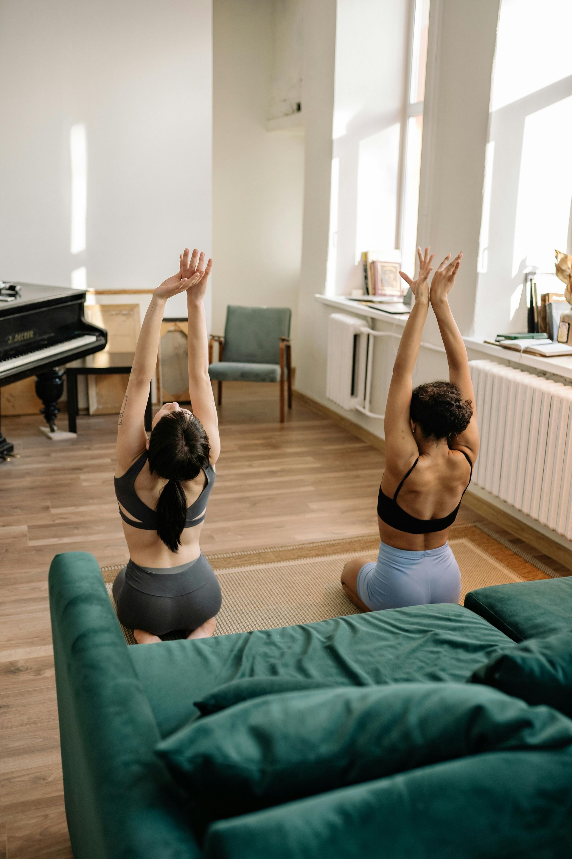 Two women are doing yoga on a couch in a living room.